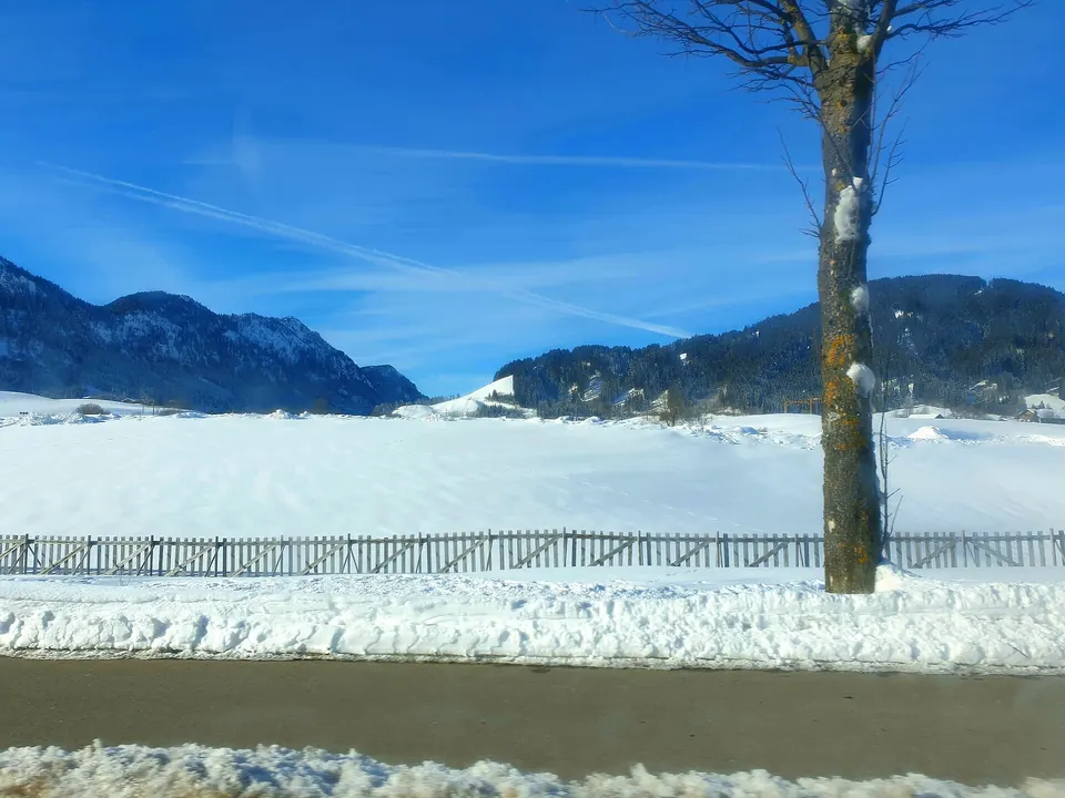 Apsnigtas kelias Austrijoje, fone kalnai ir mėlynas dangus
