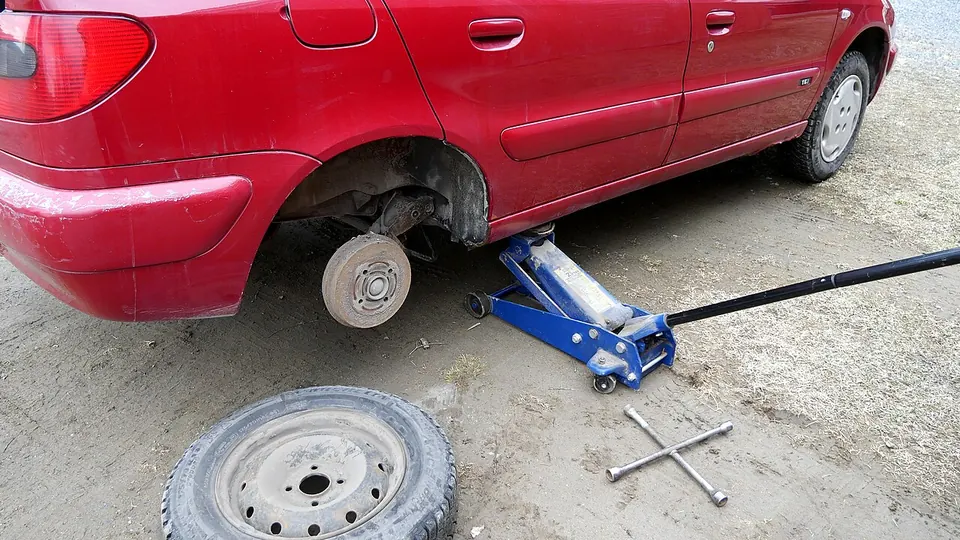 Pakeltas automobilis su nuimtu ratu, šalia padanga ir domkratas